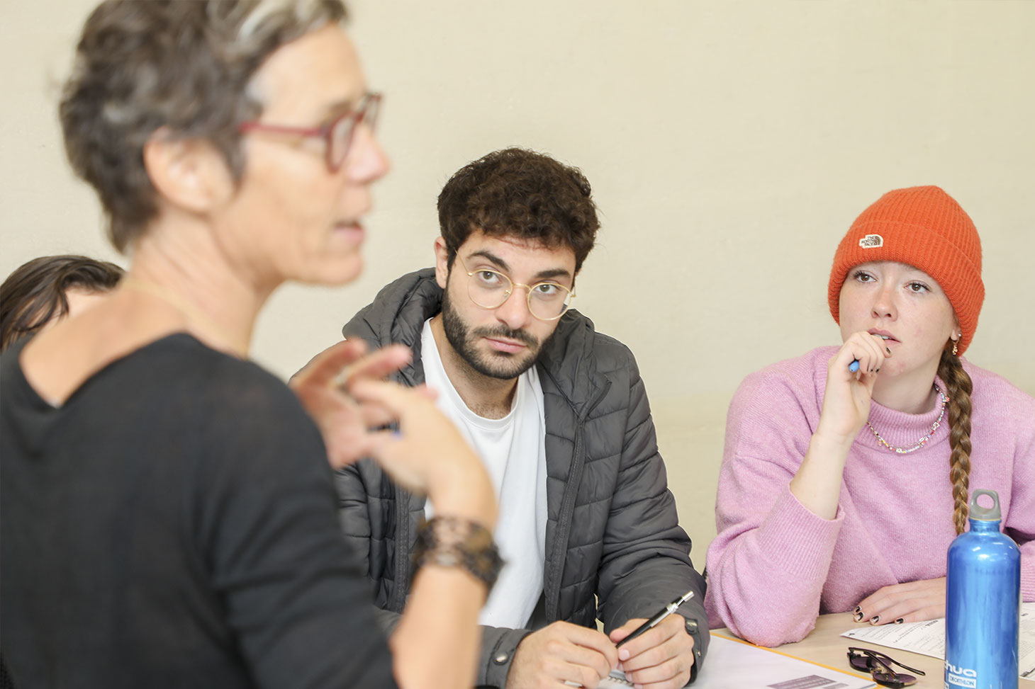 Un étudiant et une étudiante écoutent une enseignante dans une salle de classe